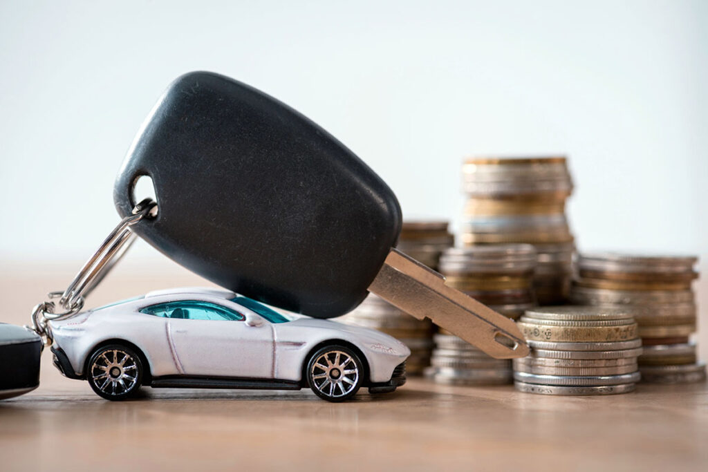 A car key sits on top of a toy car on a table along with a pile of coins.