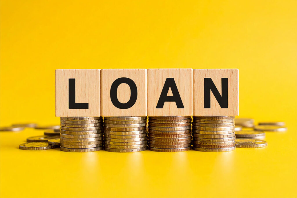 Blocks spelling "LOAN" are positioned in front of stacks of coins, against a bright yellow background.