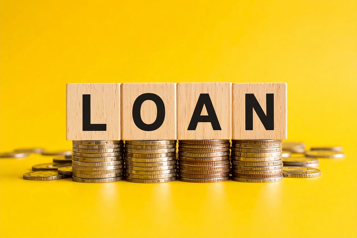 Blocks spelling "LOAN" are positioned in front of stacks of coins, against a bright yellow background.