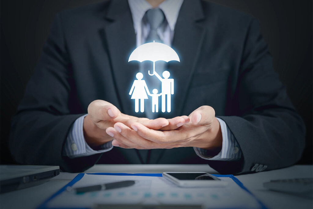 A businessman in a suit holds his hands open, with a glowing graphic of a family under an umbrella floating above them, symbolizing protection and care.