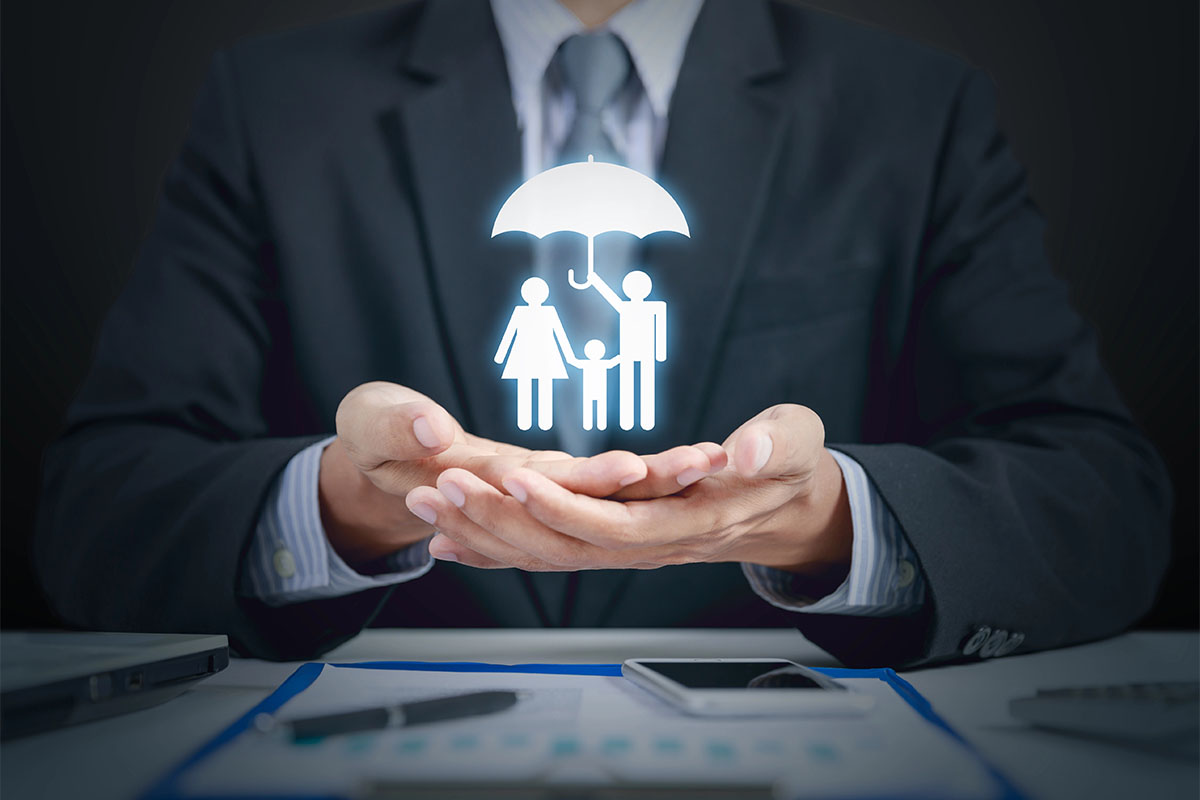 A businessman in a suit holds his hands open, with a glowing graphic of a family under an umbrella floating above them, symbolizing protection and care.