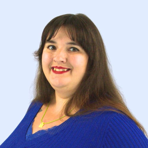 A woman with long dark hair smiles while wearing a blue sweater and a green necklace, set against a light blue background.